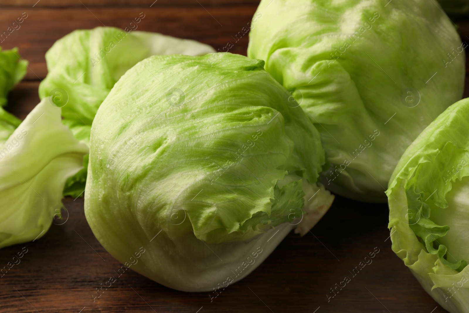 Photo of Fresh green iceberg lettuce heads and leaves on wooden table, closeup