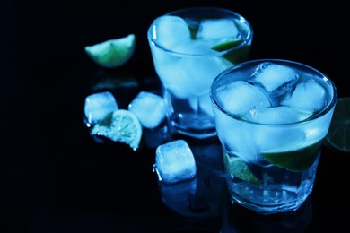 Shot glasses of vodka with ice cubes and lime slices on dark background, space for text