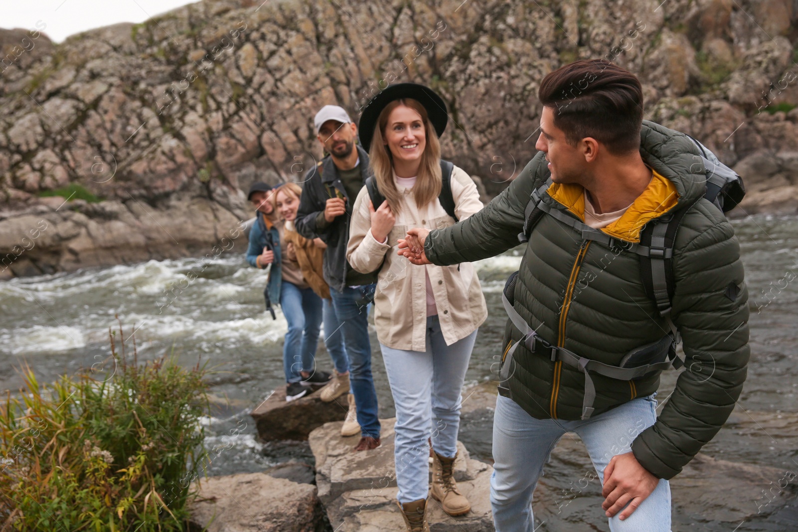 Photo of Group of friends with backpacks crossing mountain river on autumn day