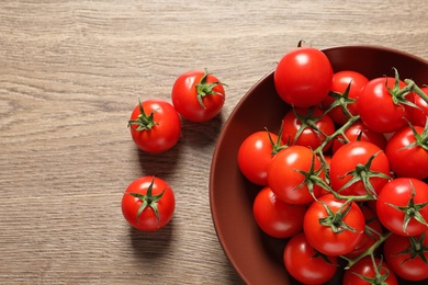 Photo of Plate with fresh cherry tomatoes on wooden background, top view