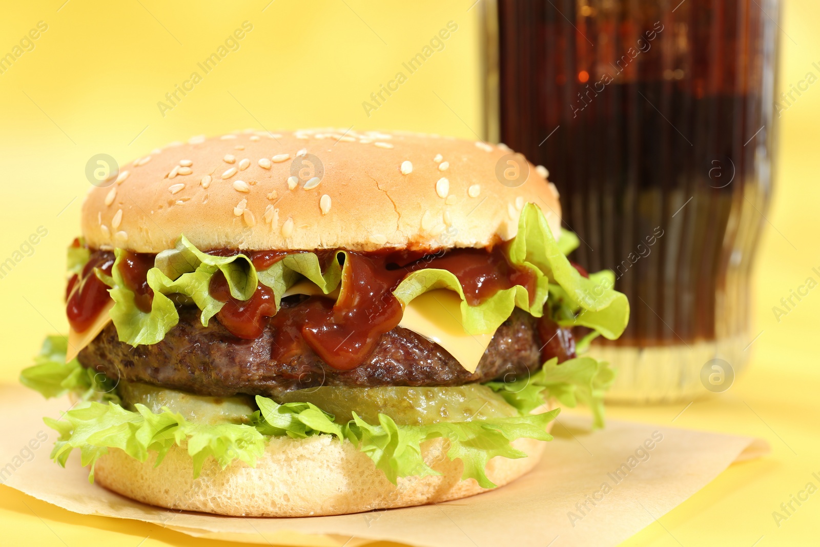 Photo of Burger with delicious patty and soda drink on yellow background, closeup