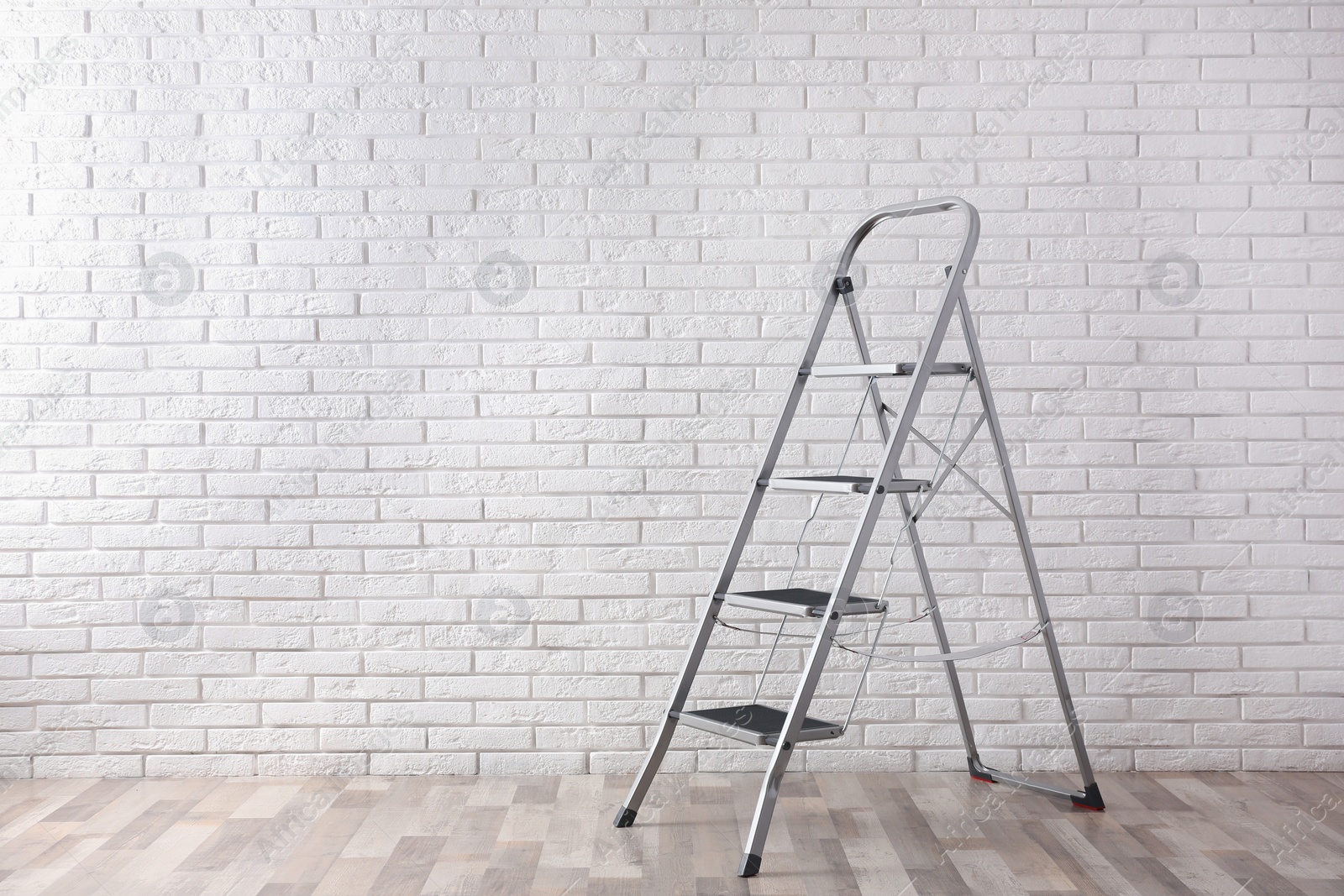 Photo of Modern metal stepladder near white brick wall indoors. Space for text