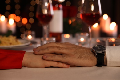 Couple holding hands together at table during romantic dinner in restaurant, closeup