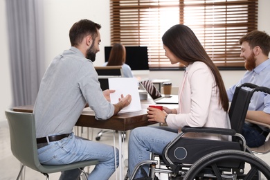 Young woman in wheelchair with colleagues at workplace