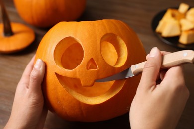 Woman carving pumpkin for Halloween at wooden table, closeup