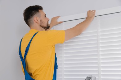 Photo of Worker in uniform installing horizontal window blinds indoors