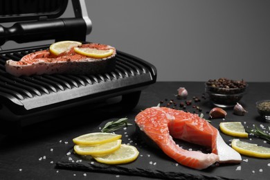 Photo of Cooking salmon. Grill, fresh fish steaks, lemon and spices on dark table