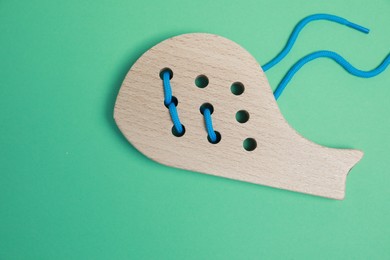 Photo of Wooden whale figure with holes and lace on green background, top view. Educational toy for motor skills development