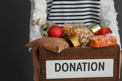 Photo of Woman holding donation box with food on gray background, closeup