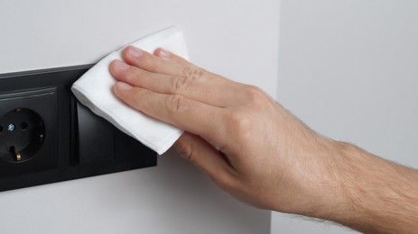 Photo of Man cleaning light switch with wet wipe indoors, closeup. Protective measures