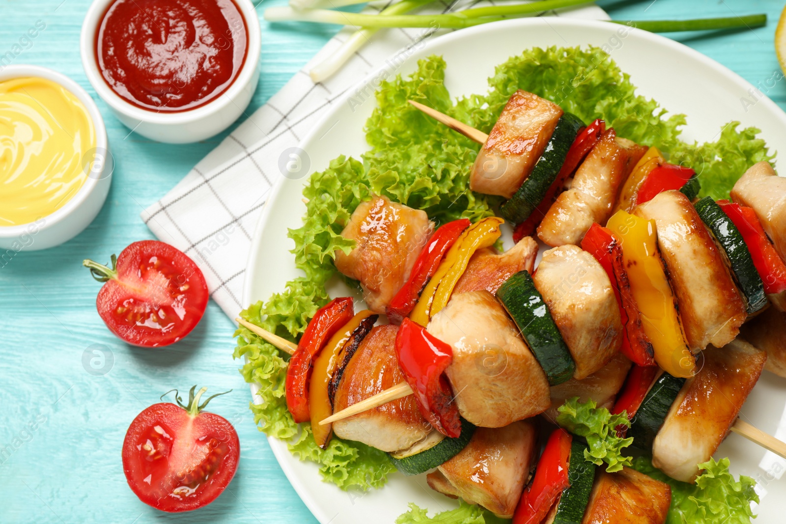 Photo of Delicious chicken shish kebabs with vegetables and sauce on light blue wooden table, closeup