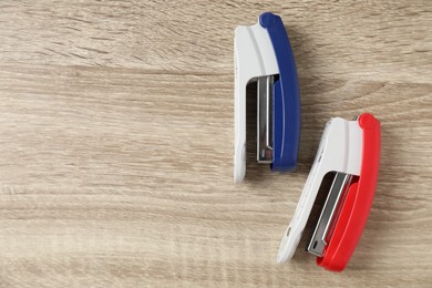 Photo of Color staplers on wooden table, flat lay. Space for text