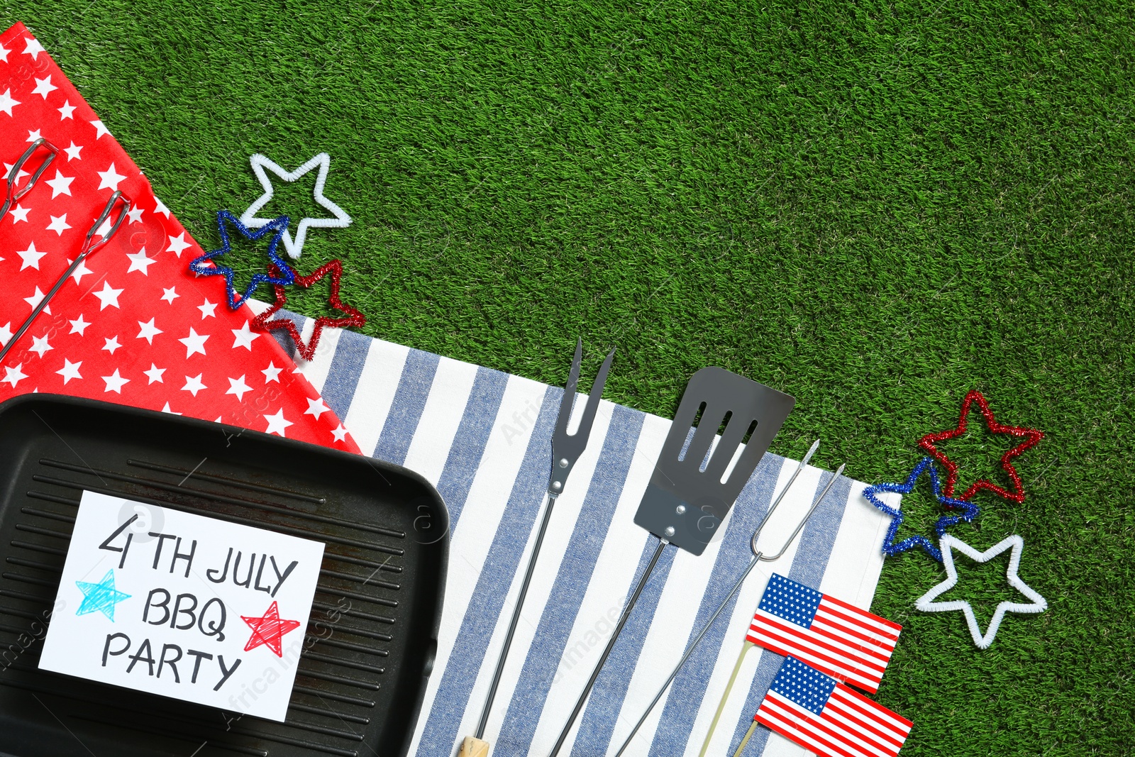 Photo of Flat lay composition with barbecue tools, card and grill pan on green grass, space for text. USA Independence Day