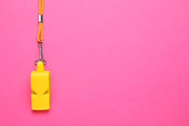 Photo of One yellow whistle with cord on pink background, top view. Space for text