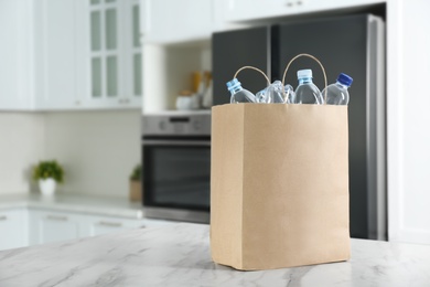 Paper bag with used plastic bottles on table in kitchen, space for text. Recycling problem