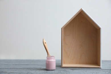 Photo of Brush with paint and wooden house model on grey table. Space for text