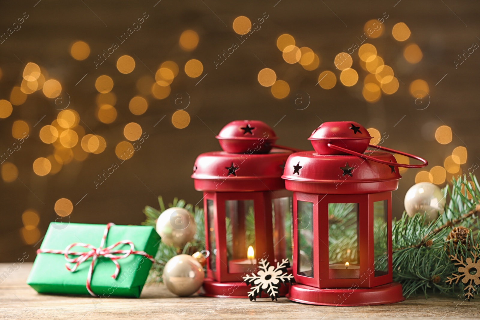 Photo of Composition with lanterns and decorated fir branches on table against blurred background. Winter holidays