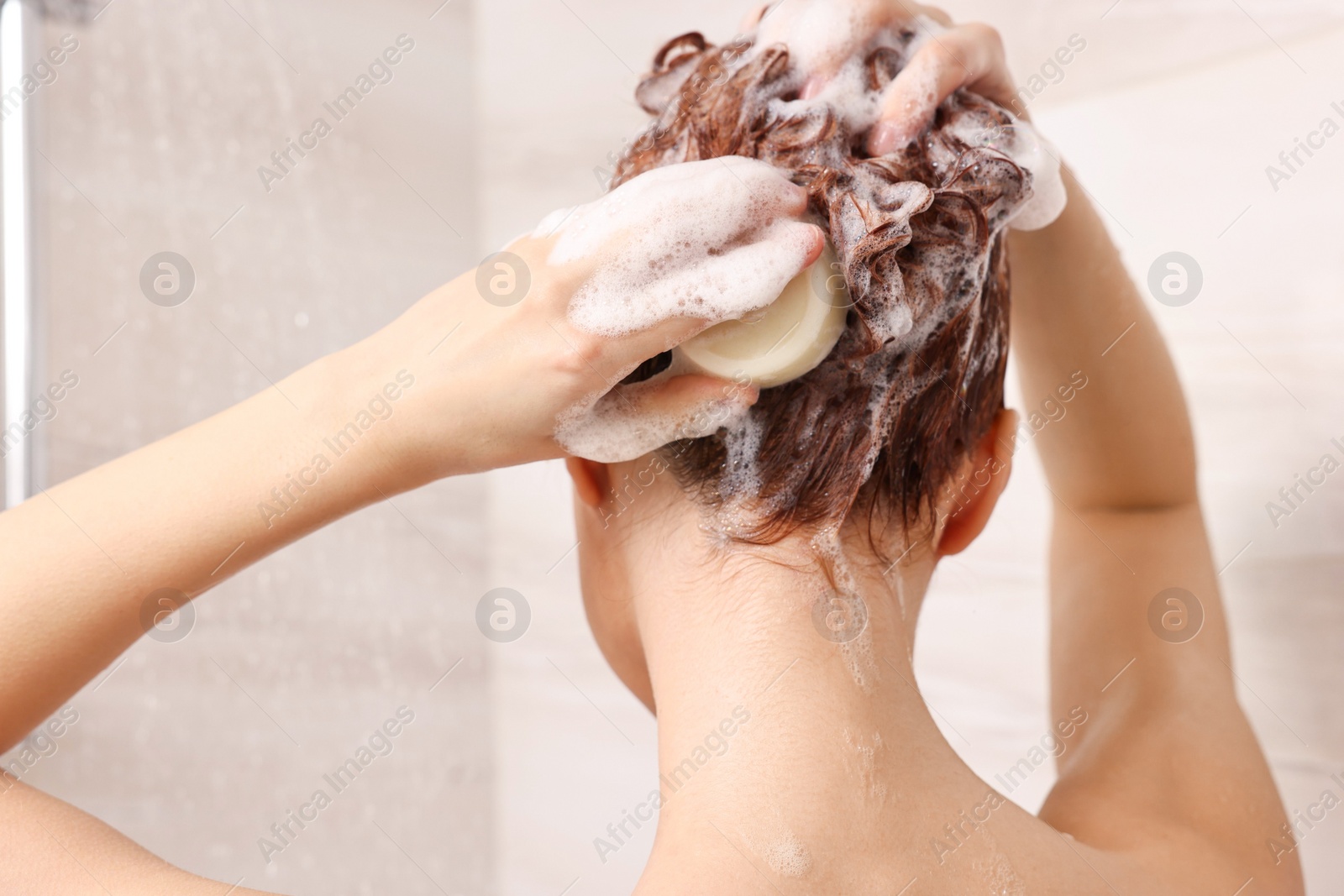 Photo of Young woman washing her hair with solid shampoo bar in shower, back view
