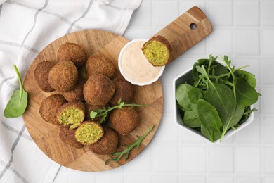 Photo of Delicious falafel balls, herbs and sauce on white tiled table, top view