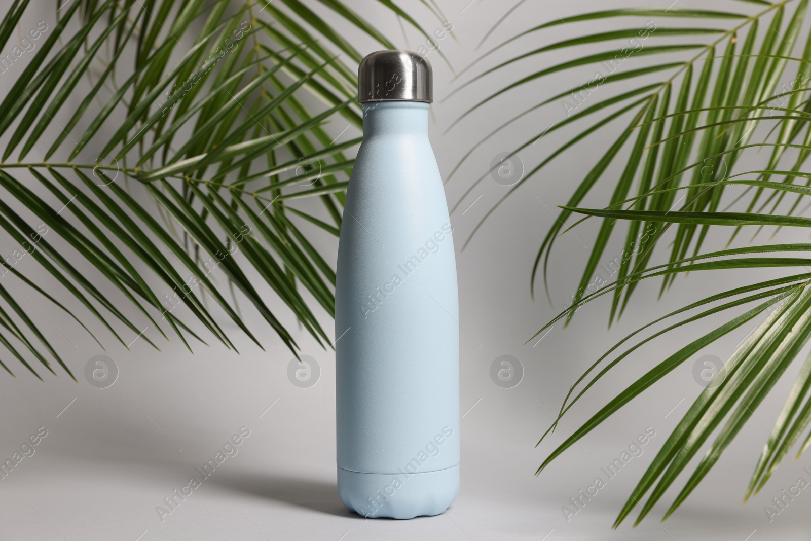 Photo of Stylish thermo bottle near tropical leaves on light grey background