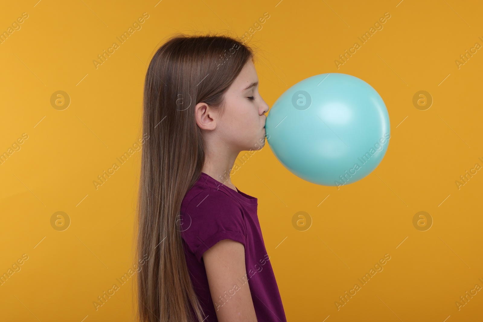 Photo of Girl inflating bright balloon on orange background