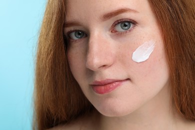Photo of Beautiful woman with freckles and cream on her face against light blue background, closeup