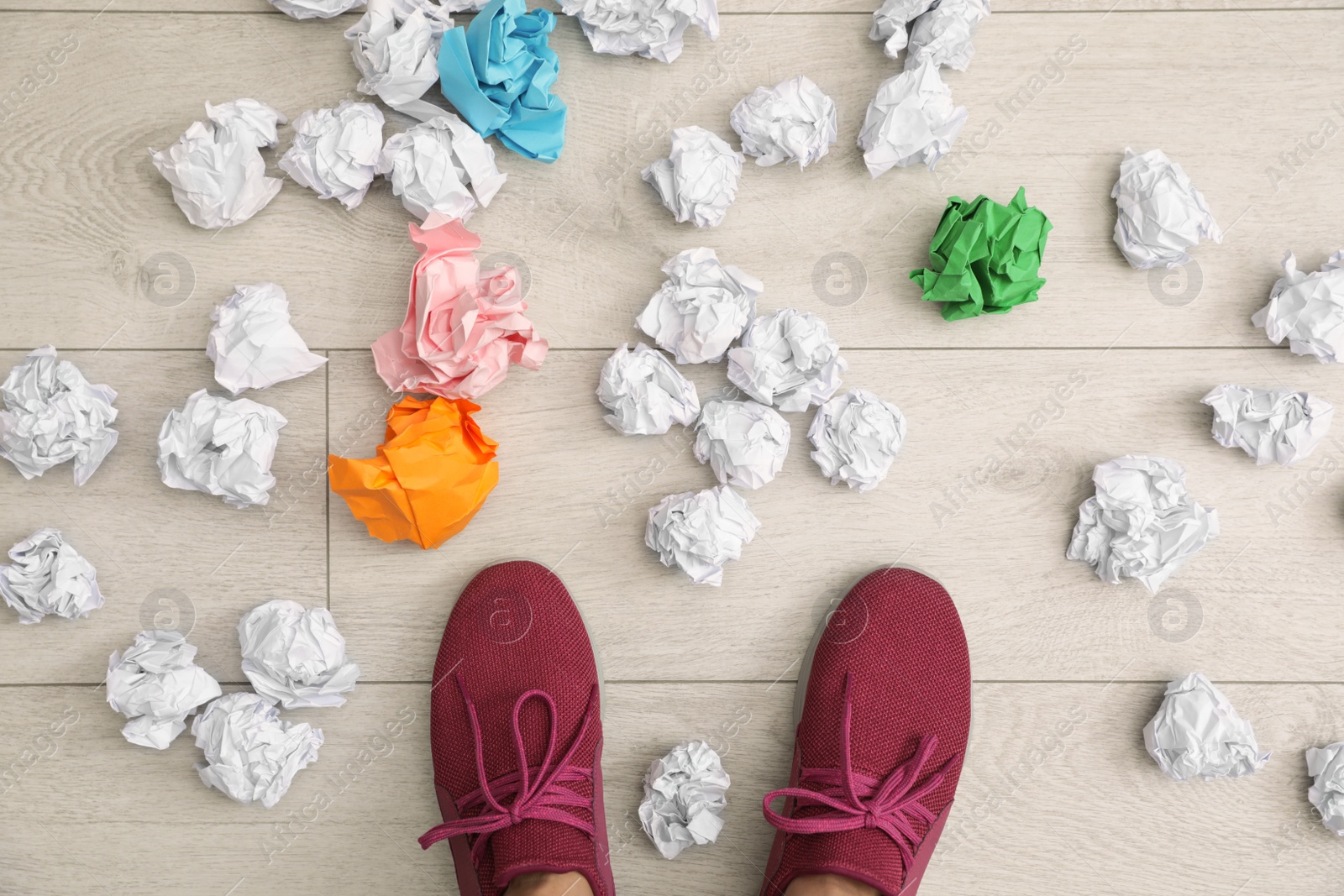 Photo of Closeup of person's feet surrounded by crumpled paper on floor, top view. Lack of ideas