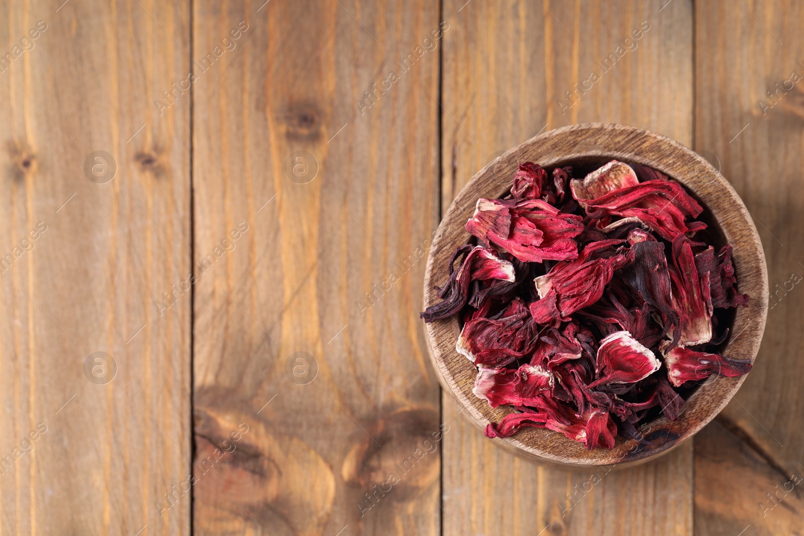 Photo of Dry hibiscus tea in bowl on wooden table, top view. Space for text