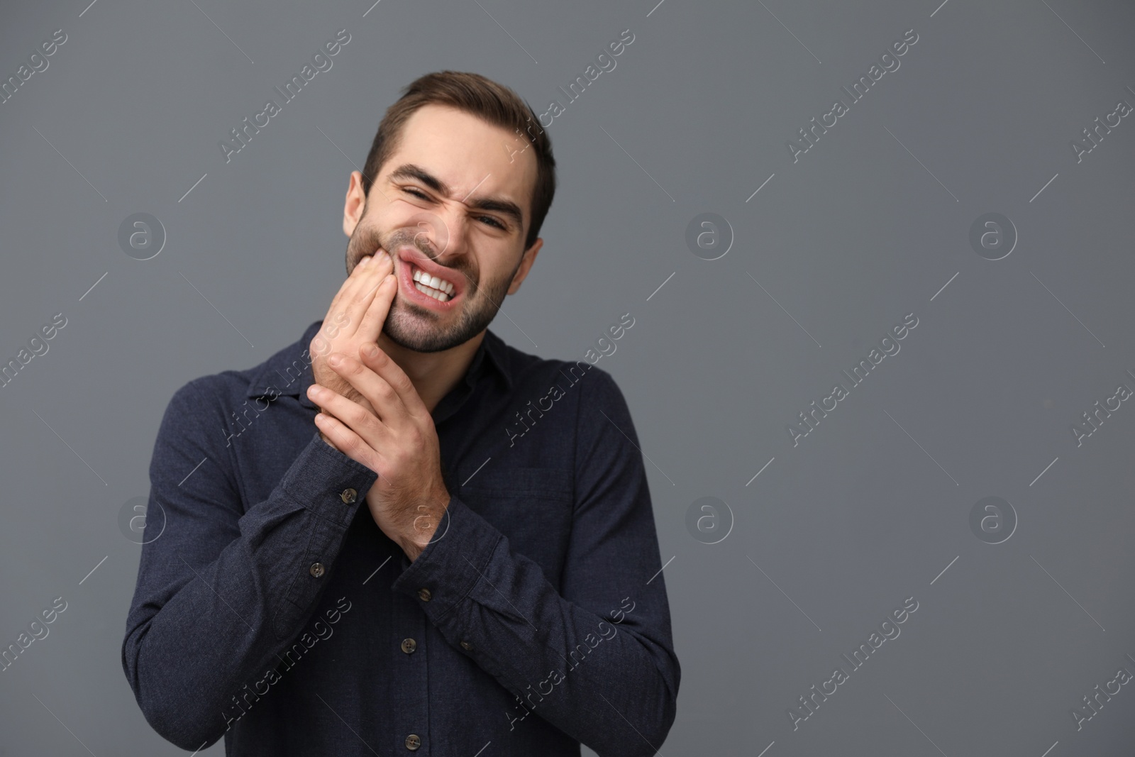 Photo of Young man suffering from strong tooth pain on grey background, space for text