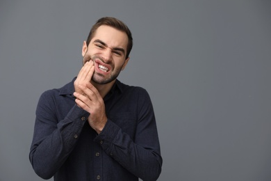 Young man suffering from strong tooth pain on grey background, space for text