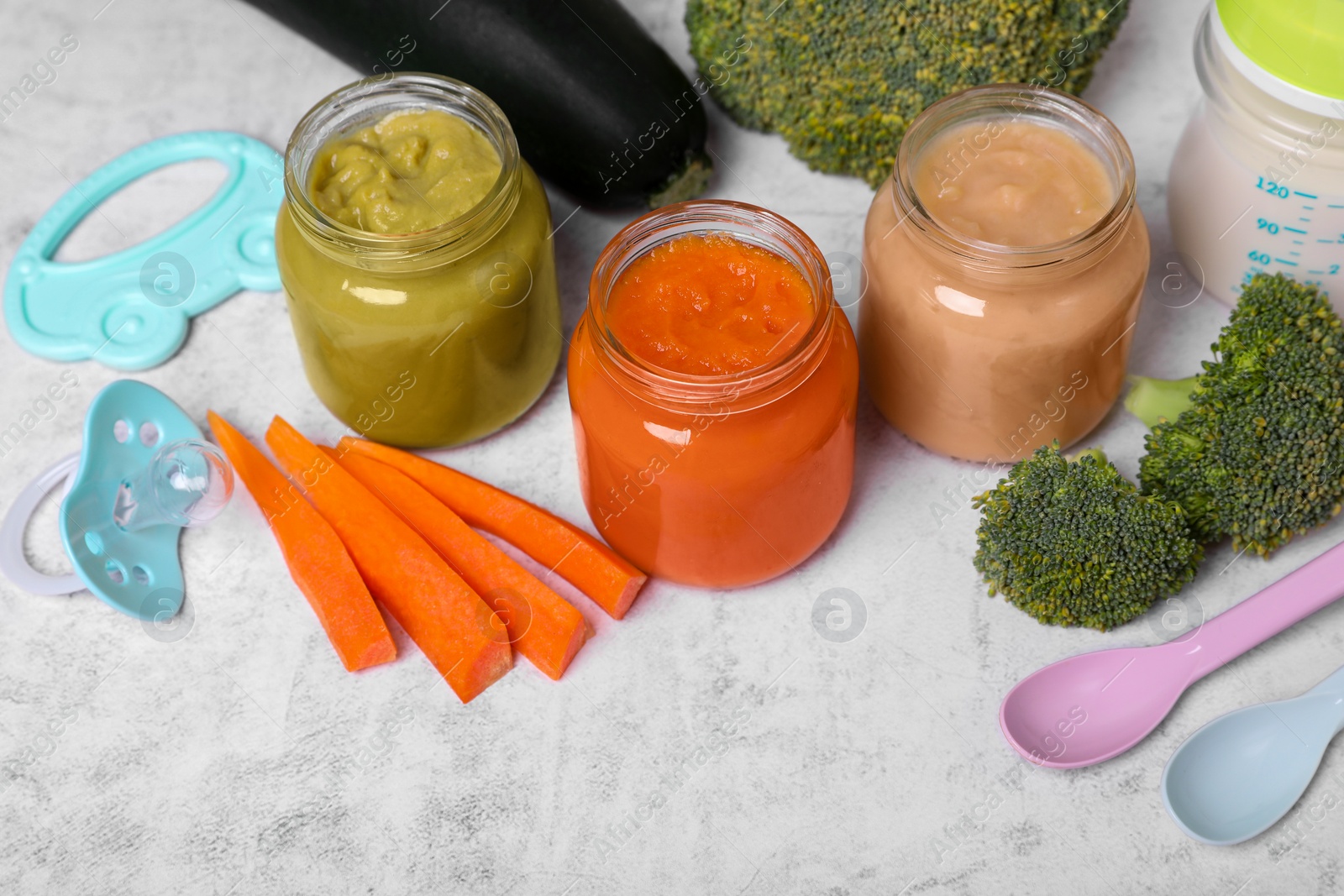 Photo of Jars with healthy baby food, spoons and ingredients on white textured table