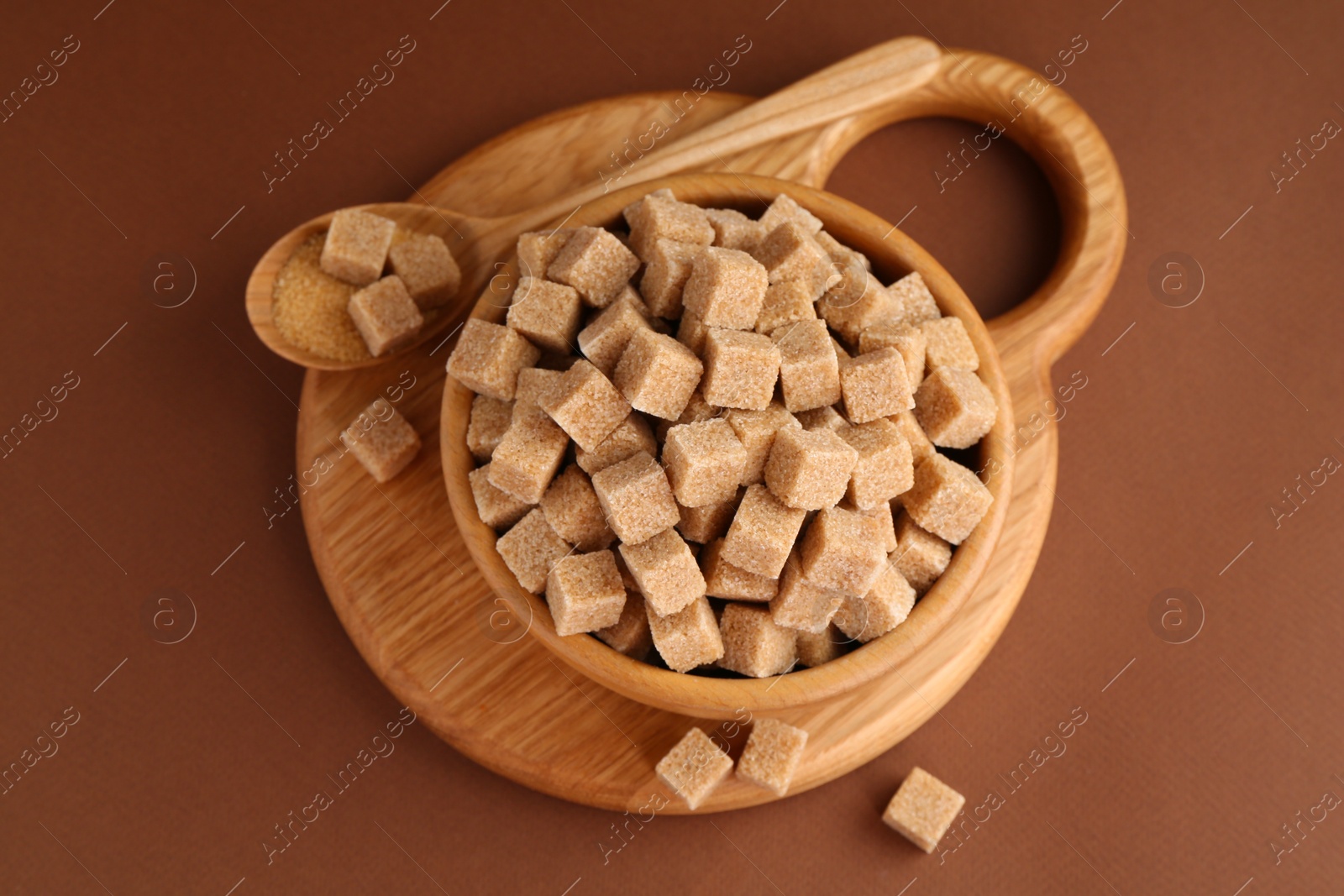 Photo of Brown sugar cubes in bowl and spoon on color background, top view