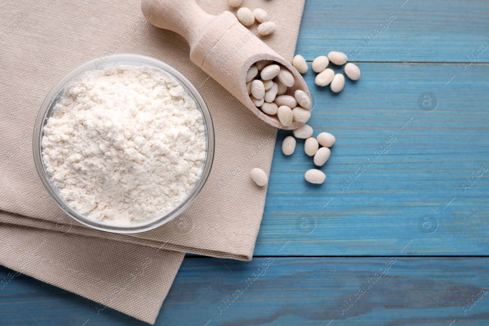 Photo of Kidney bean flour and seeds on light blue wooden table, flat lay. Space for text