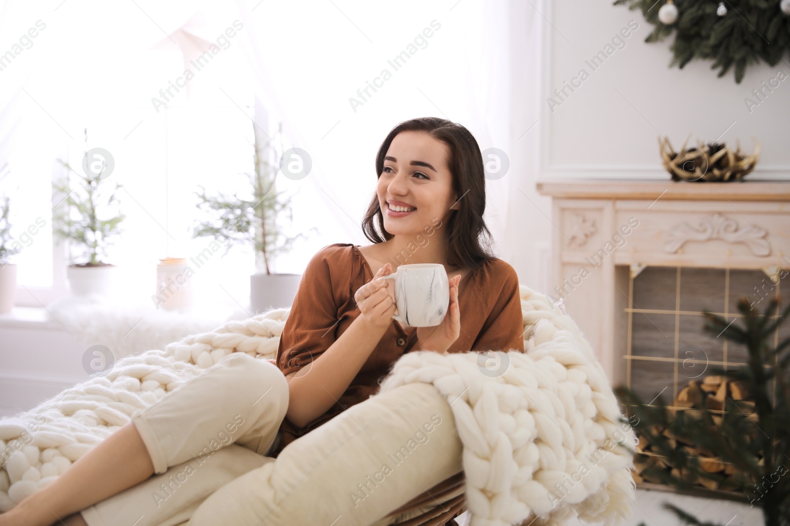 Photo of Woman with hot drink resting in comfortable papasan chair at home