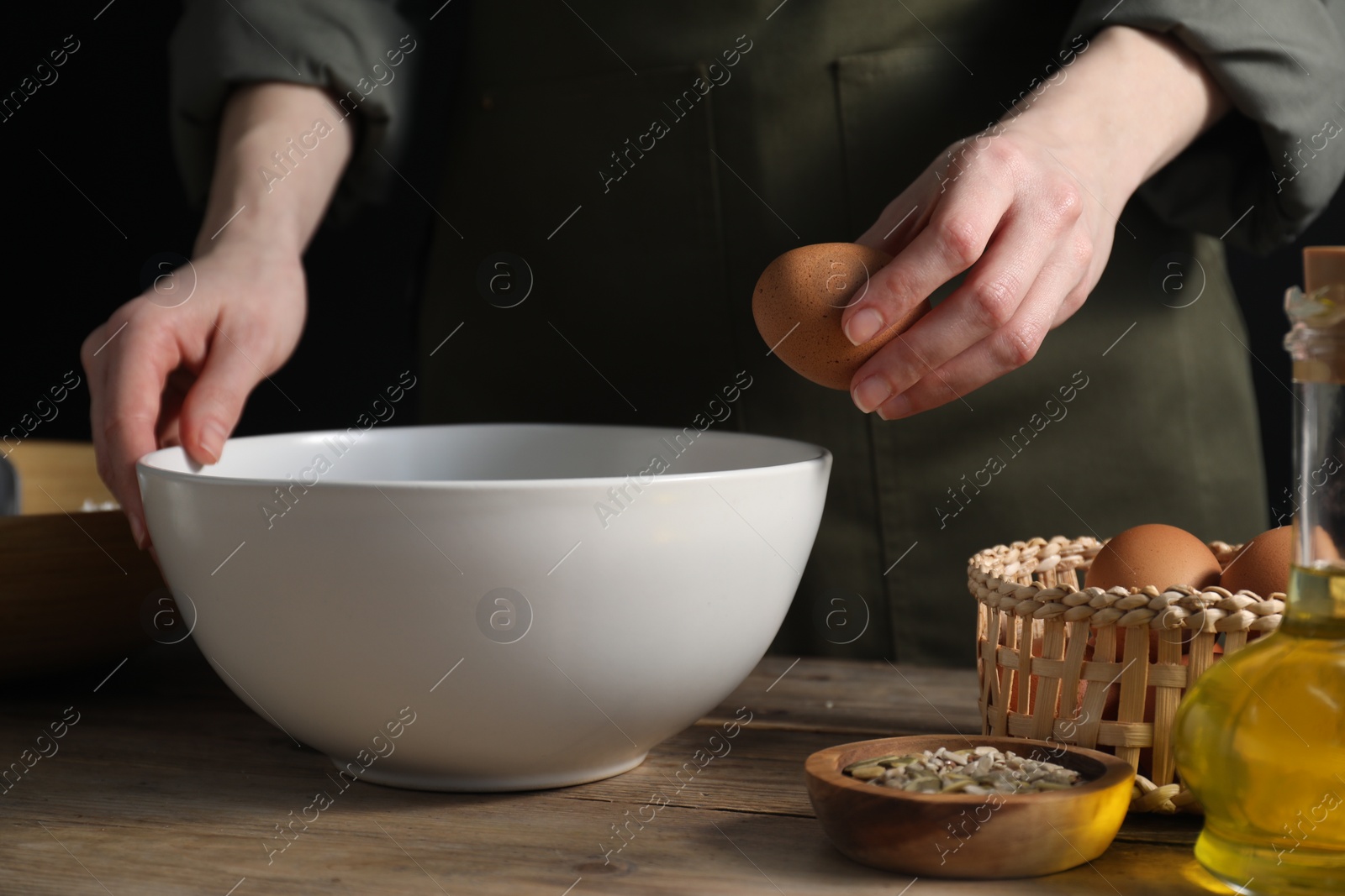 Photo of Making bread. Woman adding egg into dough at wooden table on dark background, closeup