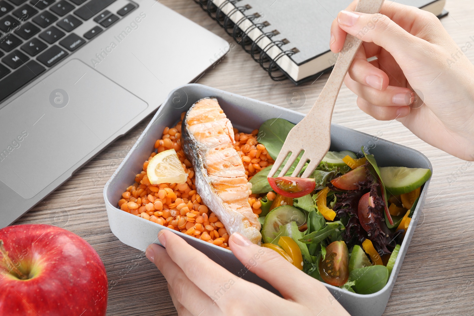 Photo of Woman eating healthy products high in vegetable fats near laptop at wooden table, closeup