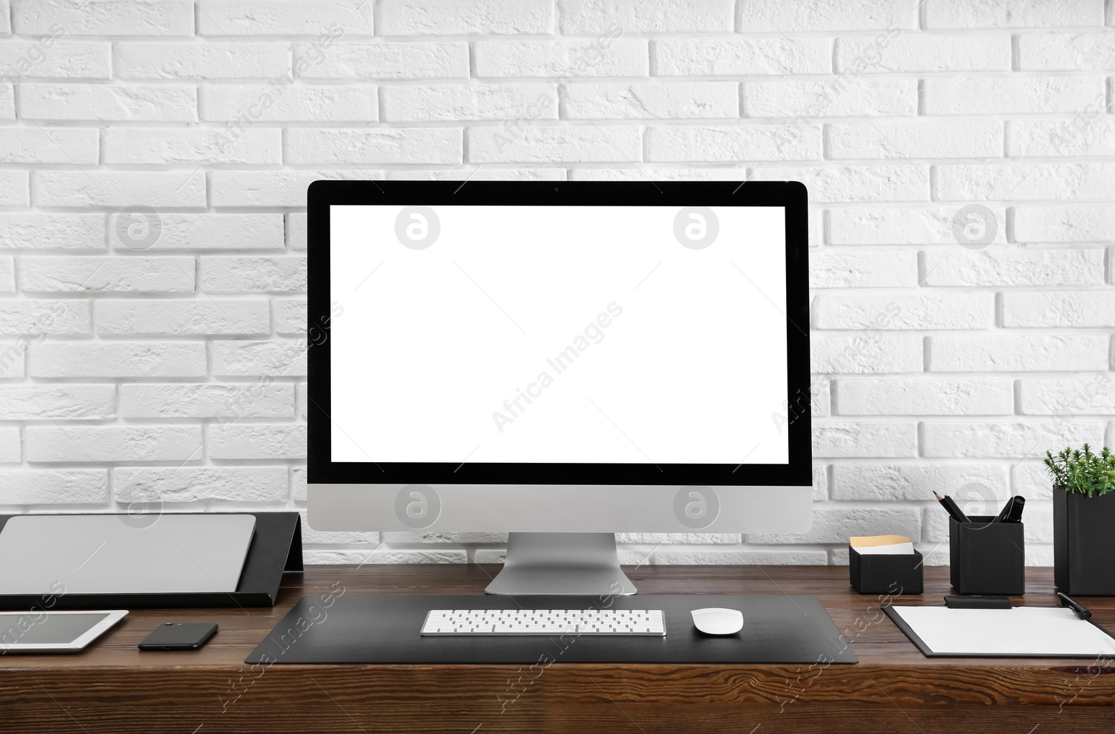 Image of Modern computer with blank screen on table near brick wall. Space for design