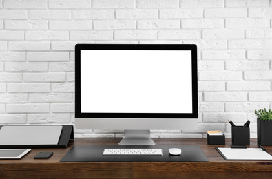 Modern computer with blank screen on table near brick wall. Space for design