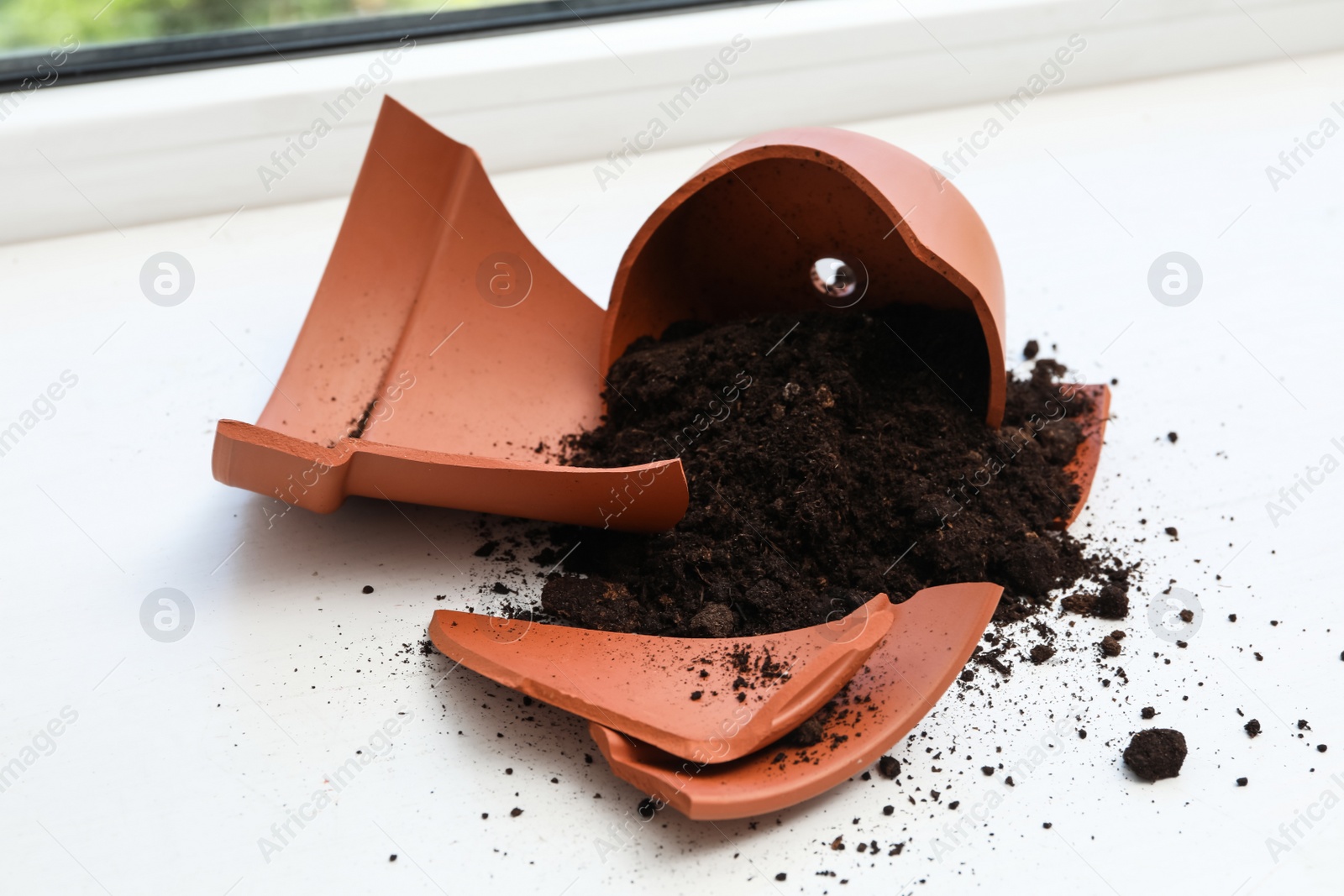 Photo of Broken terracotta flower pot with soil on white windowsill indoors