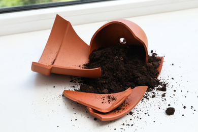 Broken terracotta flower pot with soil on white windowsill indoors