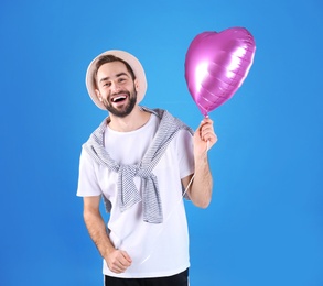 Portrait of young man with heart shaped balloon on color background