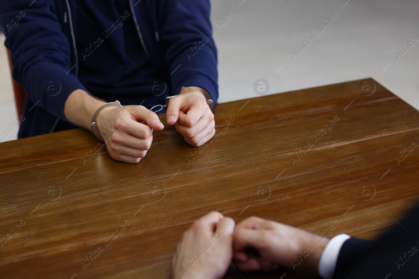 Photo of Police officer interrogating criminal in handcuffs at desk indoors