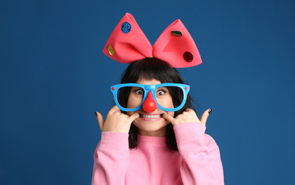 Photo of Emotional woman with funny glasses and large bow on blue background. April fool's day