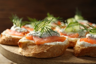 Tasty canapes with salmon, cucumber, cream cheese and dill on wooden stand, closeup