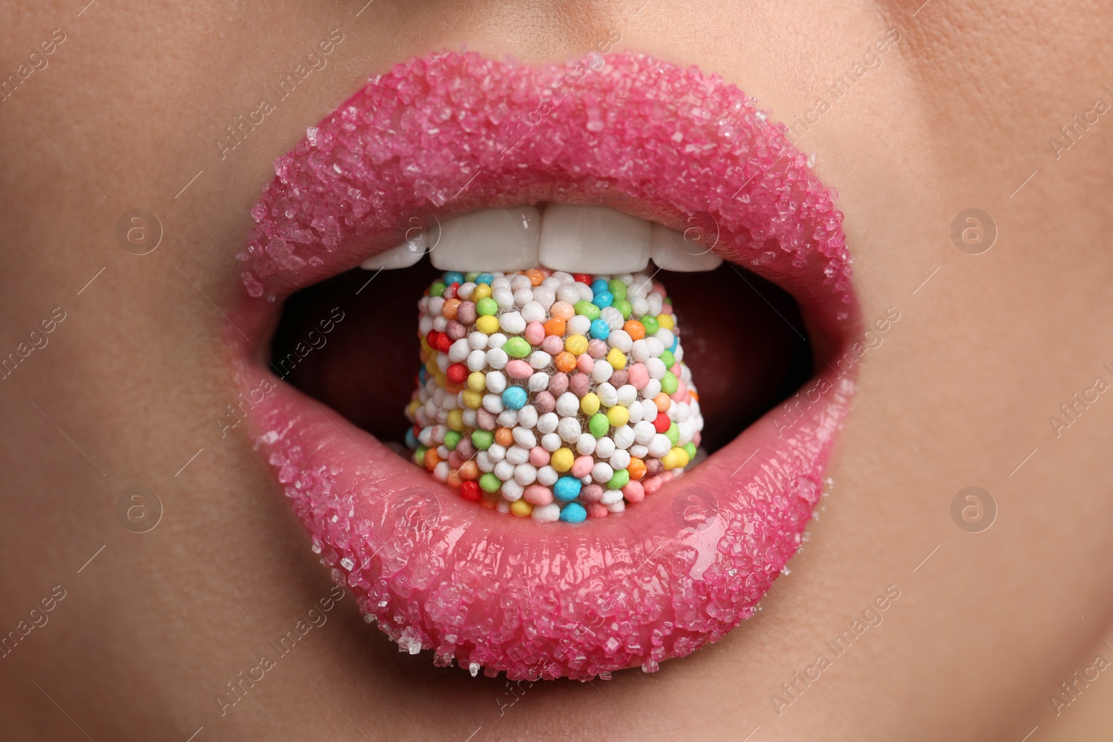 Photo of Young woman with beautiful lips covered in sugar eating candy, closeup