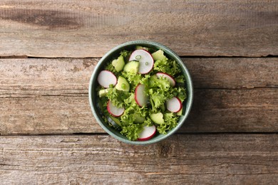 Photo of Delicious salad with radish, lettuce and cucumbers in bowl on wooden table, top view