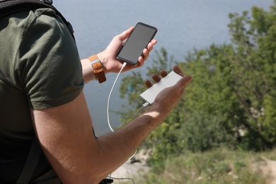 Photo of Man charging mobile phone with power bank on hill near river, closeup