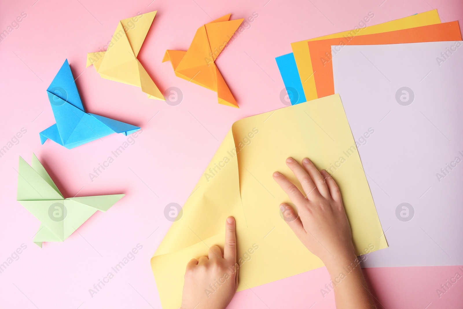 Photo of Origami art. Child folding paper on pink background, closeup and top view