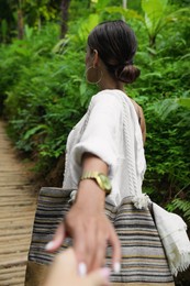 Photo of Young woman holding boyfriend's hand in green tropical park