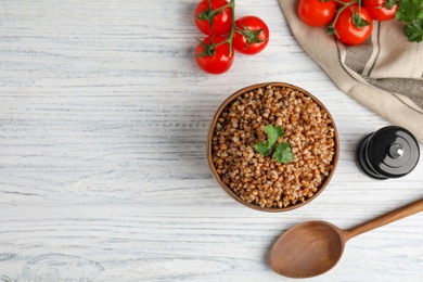 Photo of Flat lay composition with bowl of buckwheat porridge served on white wooden table. Space for text